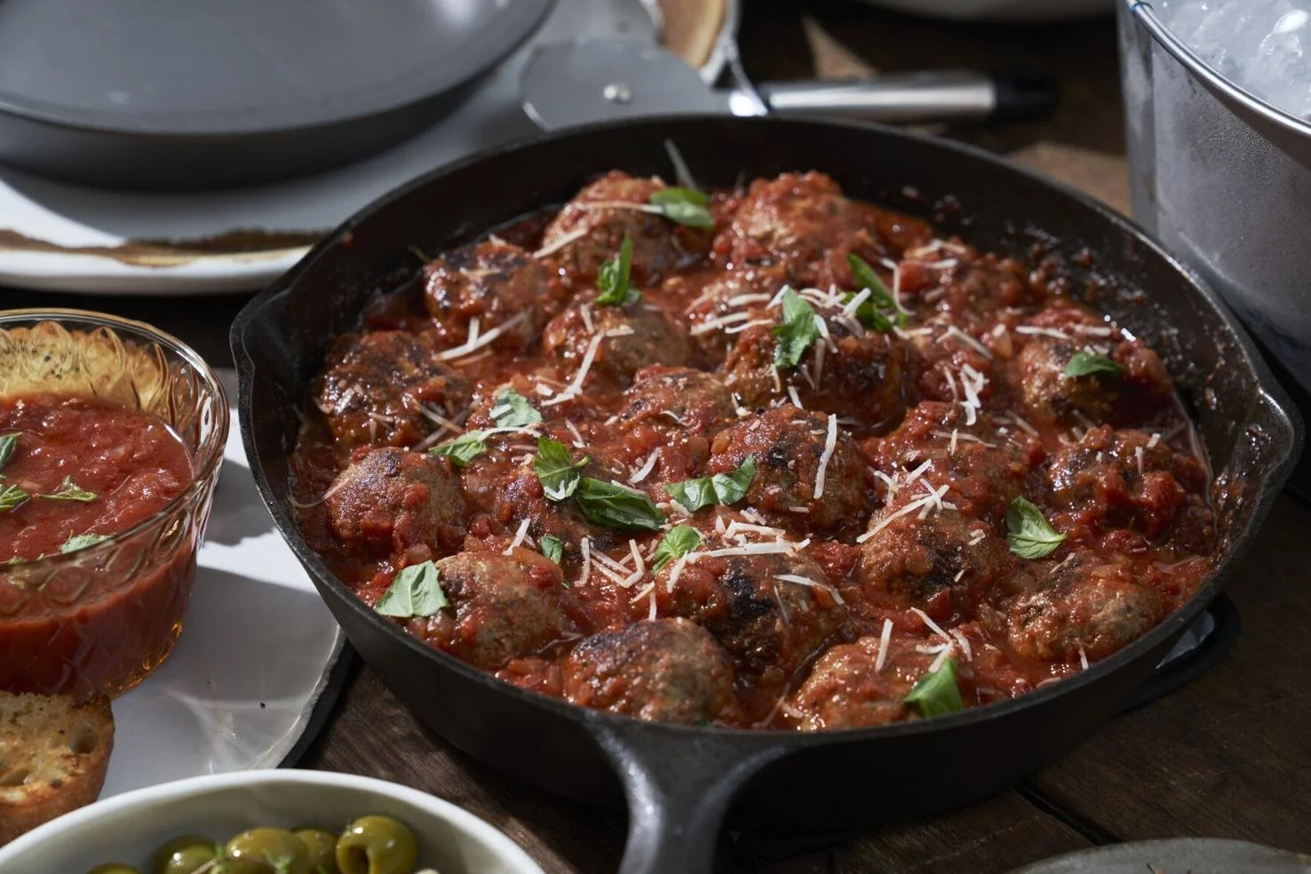 A cast iron skillet filled with meatballs in marinara sauce, garnished with fresh basil leaves and grated cheese.