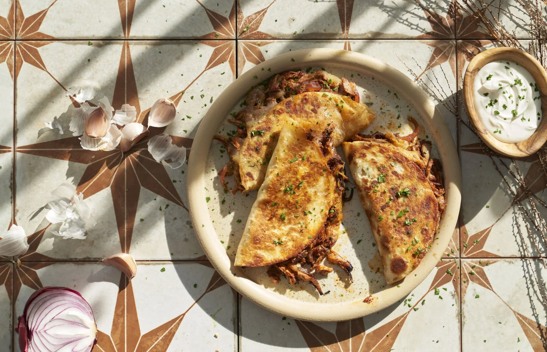 Plate of two beef quesadillas garnished with chopped herbs, served with a side of sour cream or yogurt.