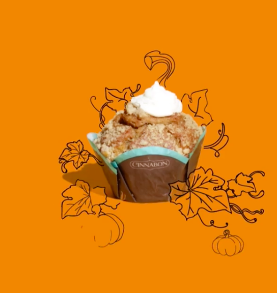 A cinnamon muffin with a dollop of whipped cream on top, surrounded by hand-drawn pumpkin and leaf illustrations on an orange background.