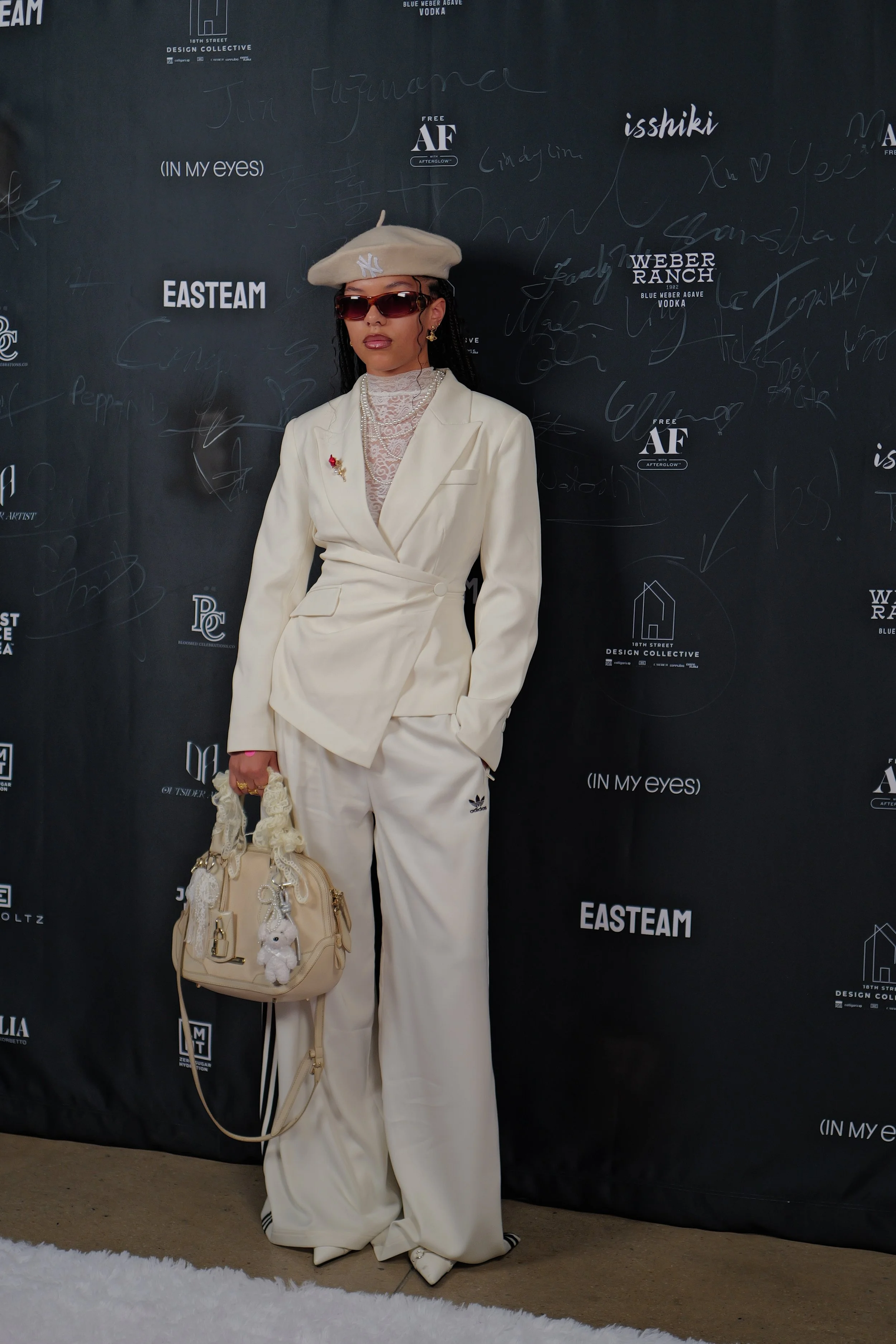 A fashion KOL in front of the photo wall featuring sponsors and supporters of the show, such as In My Eyes, 18th Street Design Collective and Weber Ranch Vodka for NYFW SS26 EASTEAM "Rebel Heiress" show by experiential production agency ANG Concept.