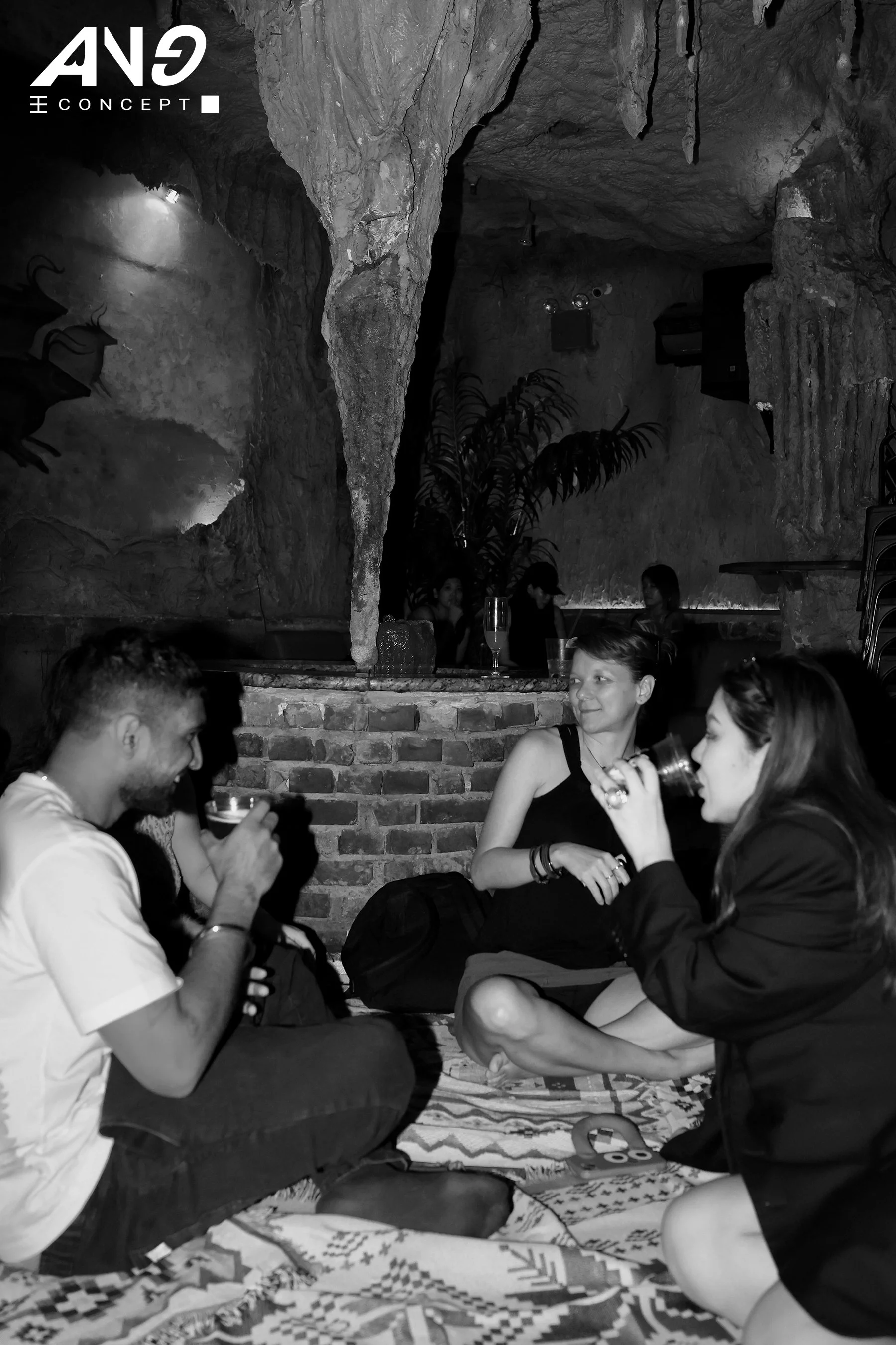 Group of people sitting on a blanket inside a cave-like venue, drinking and chatting at the ANG Lay Party in New York in August.