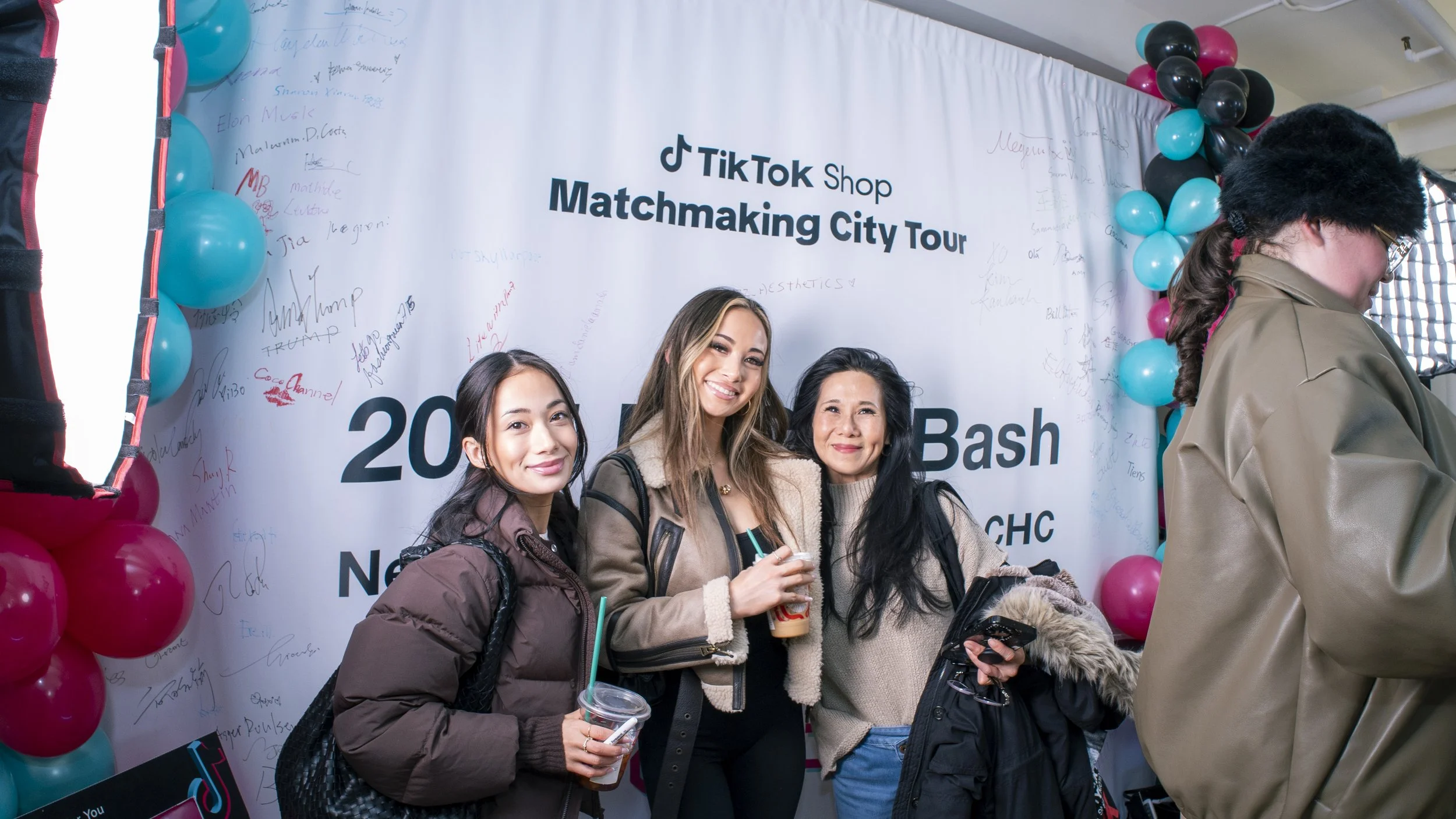 Three content creators smiling and posing for a photo at the TikTok Shop matchmaking city tour event in New York produced by ANG Concept, with a backdrop covered in famous signatures
