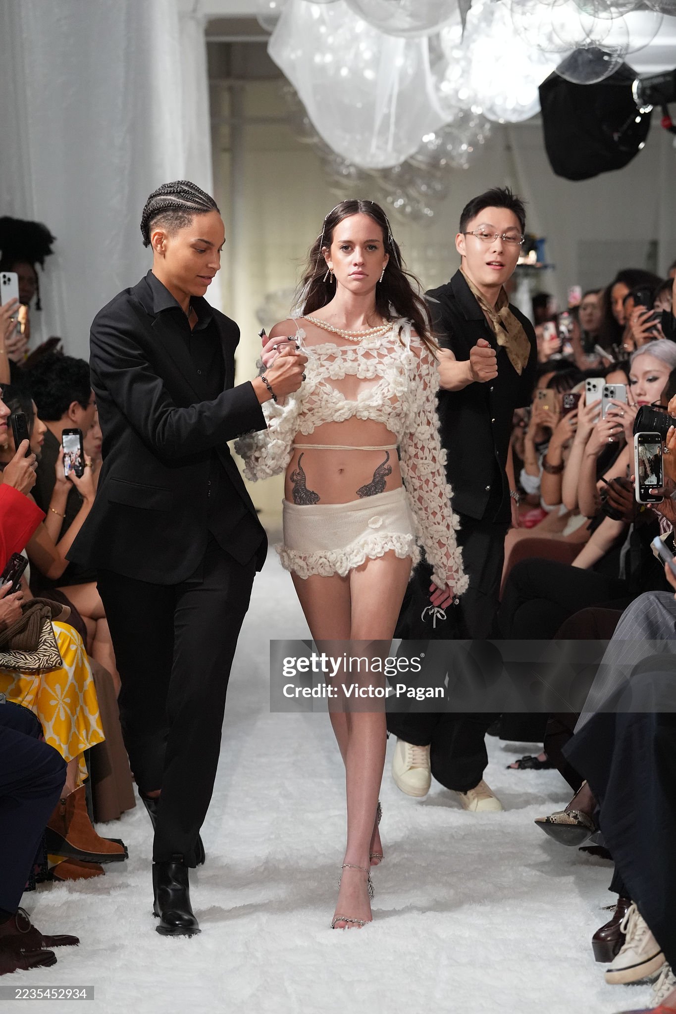 A model marching down the runway with "bodyguards" lighting up her cigarette at the NYFW SS26 EASTEAM "Rebel Heiress" show by experiential production agency ANG Concept.