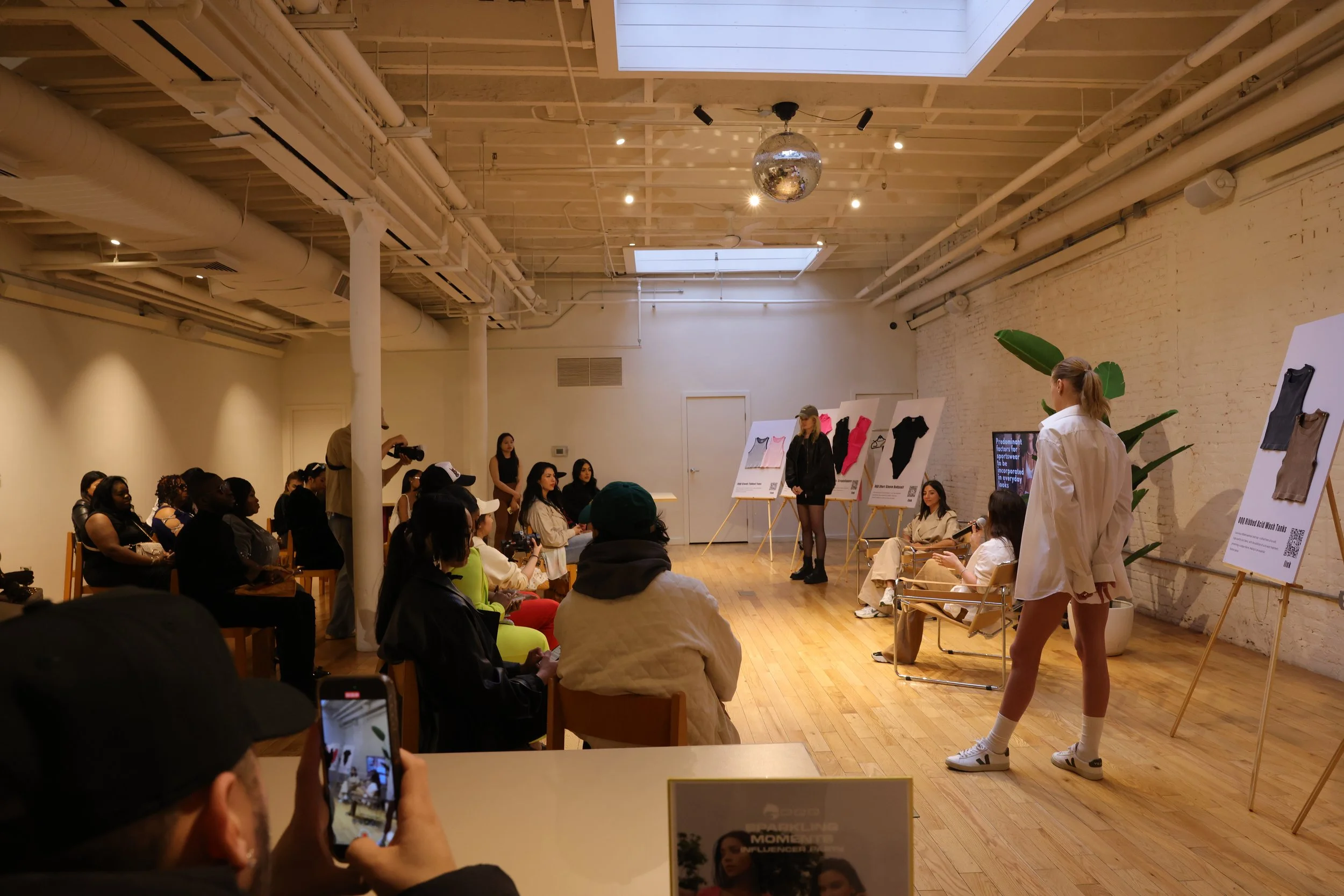 Stylists and models presenting different styling choices of OQQ's looks on easels at the brand's press conference.