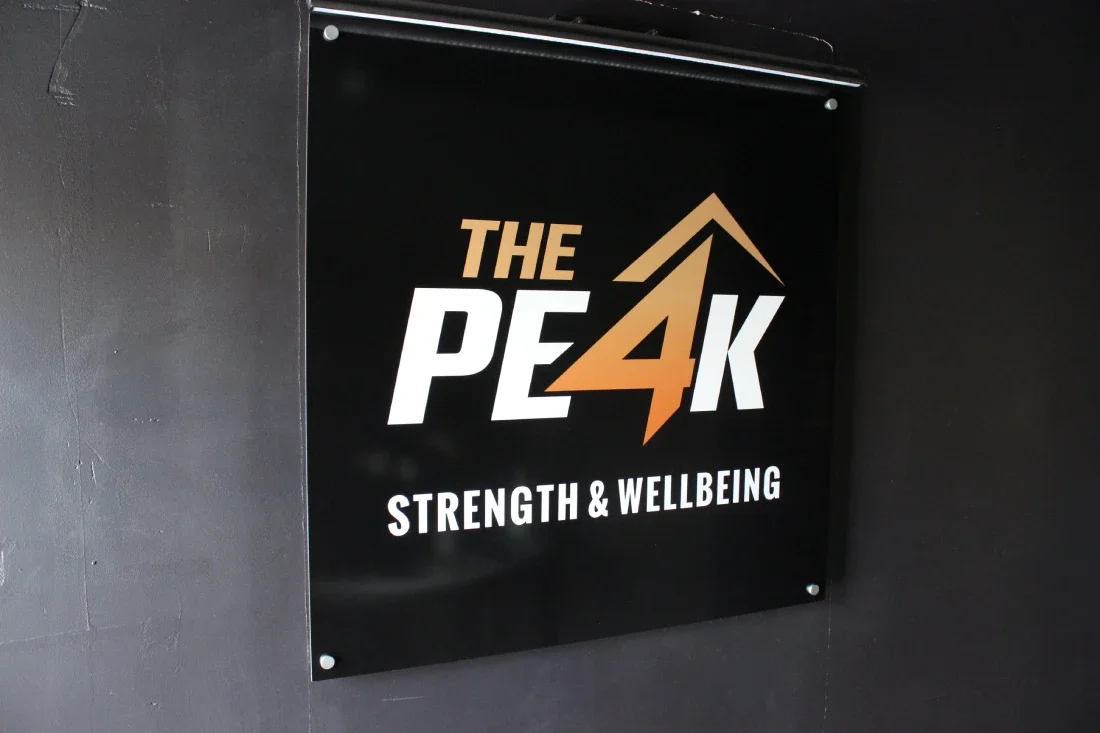 Business sign displaying the logo on a wall that reads "The Peak Strength & Wellbeing,".