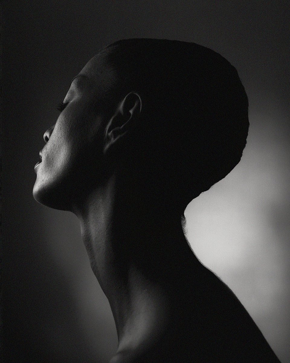 Black and white side profile of a woman with short hair, highlighting her face and neck against a dark background.