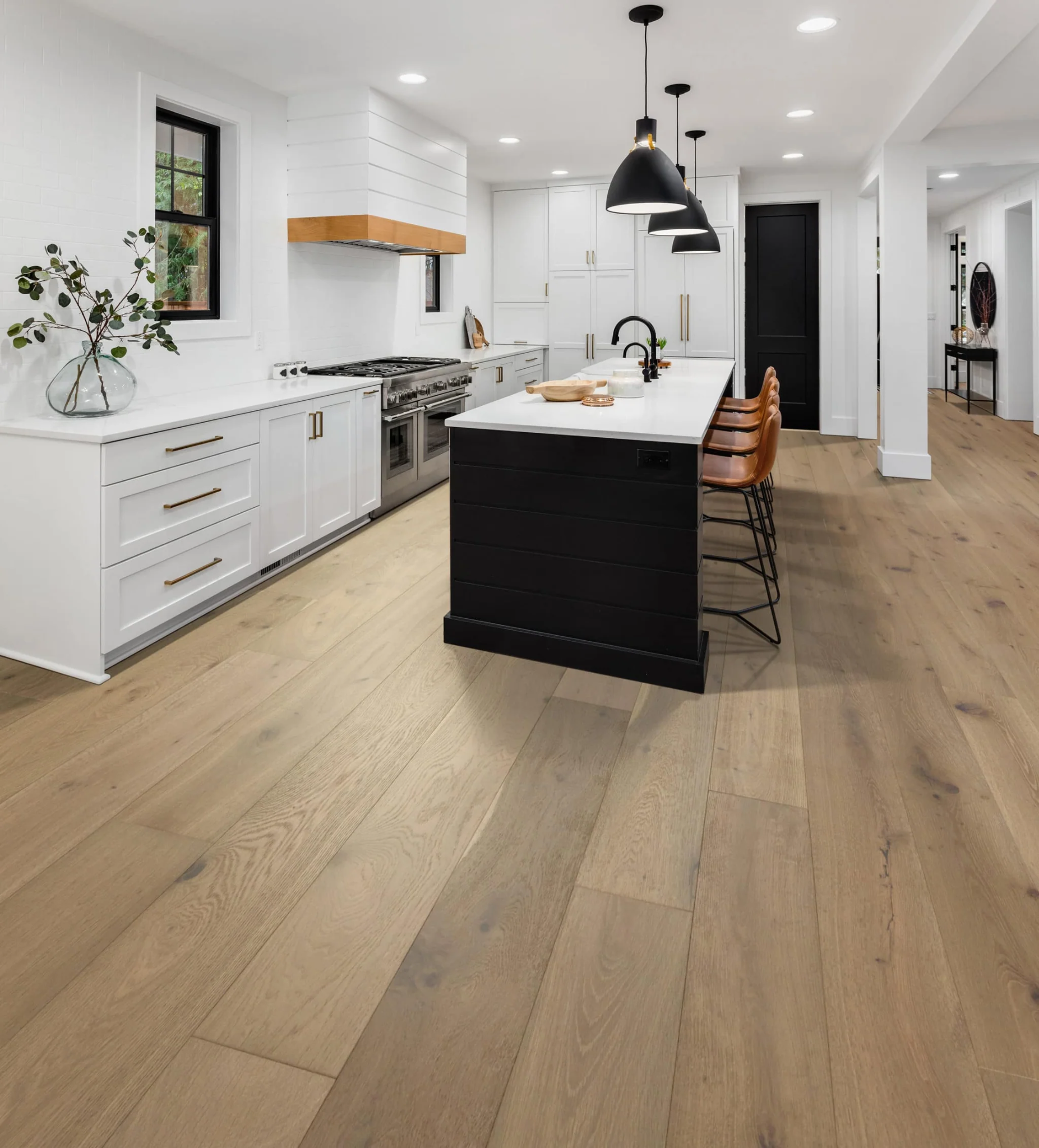 Modern kitchen with white cabinets, black island, wooden flooring, pendant lights, and a vase with a plant.