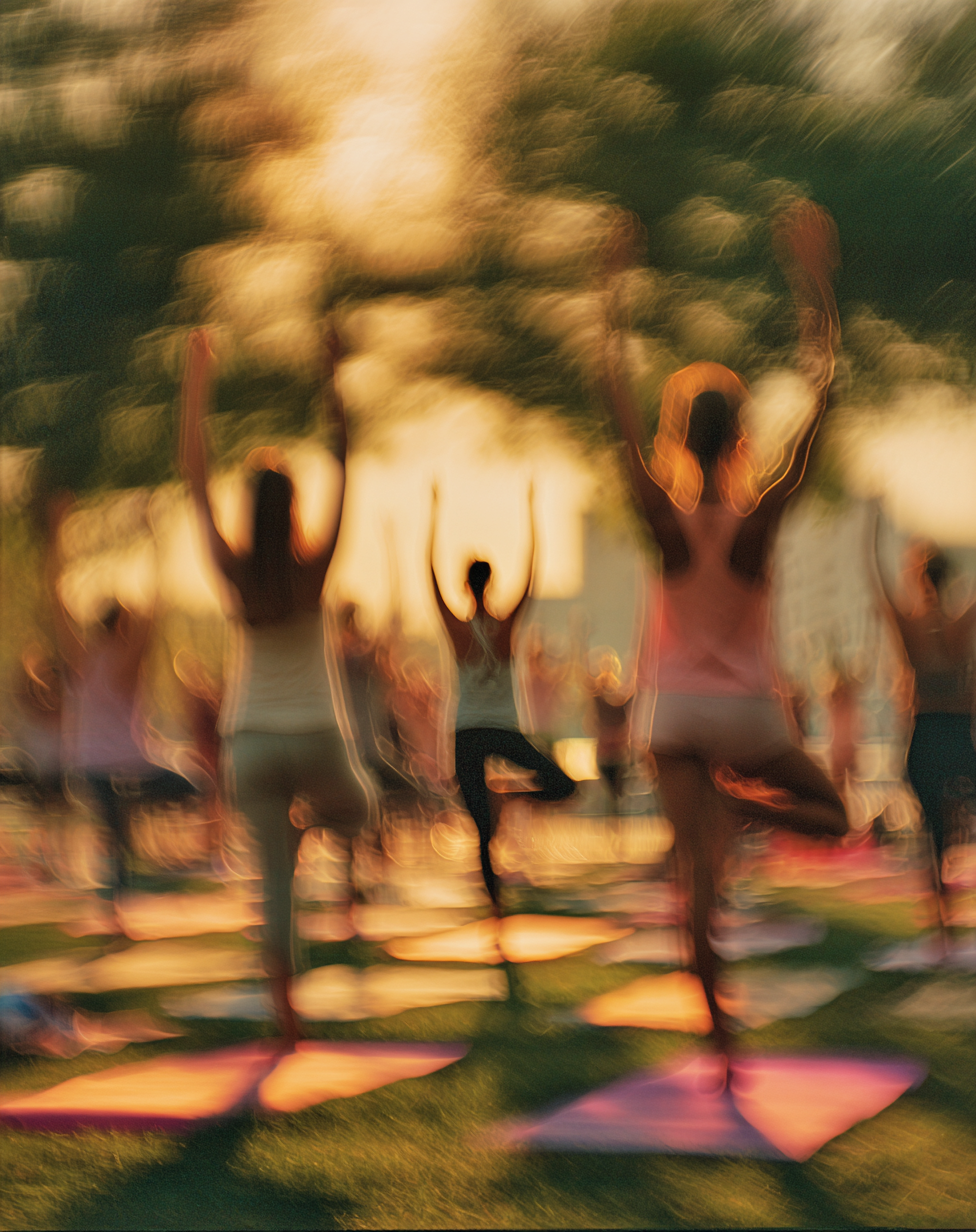 Personas haciendo yoga al aire libre en una puesta de sol, en movimiento y con cierta falta de enfoque.