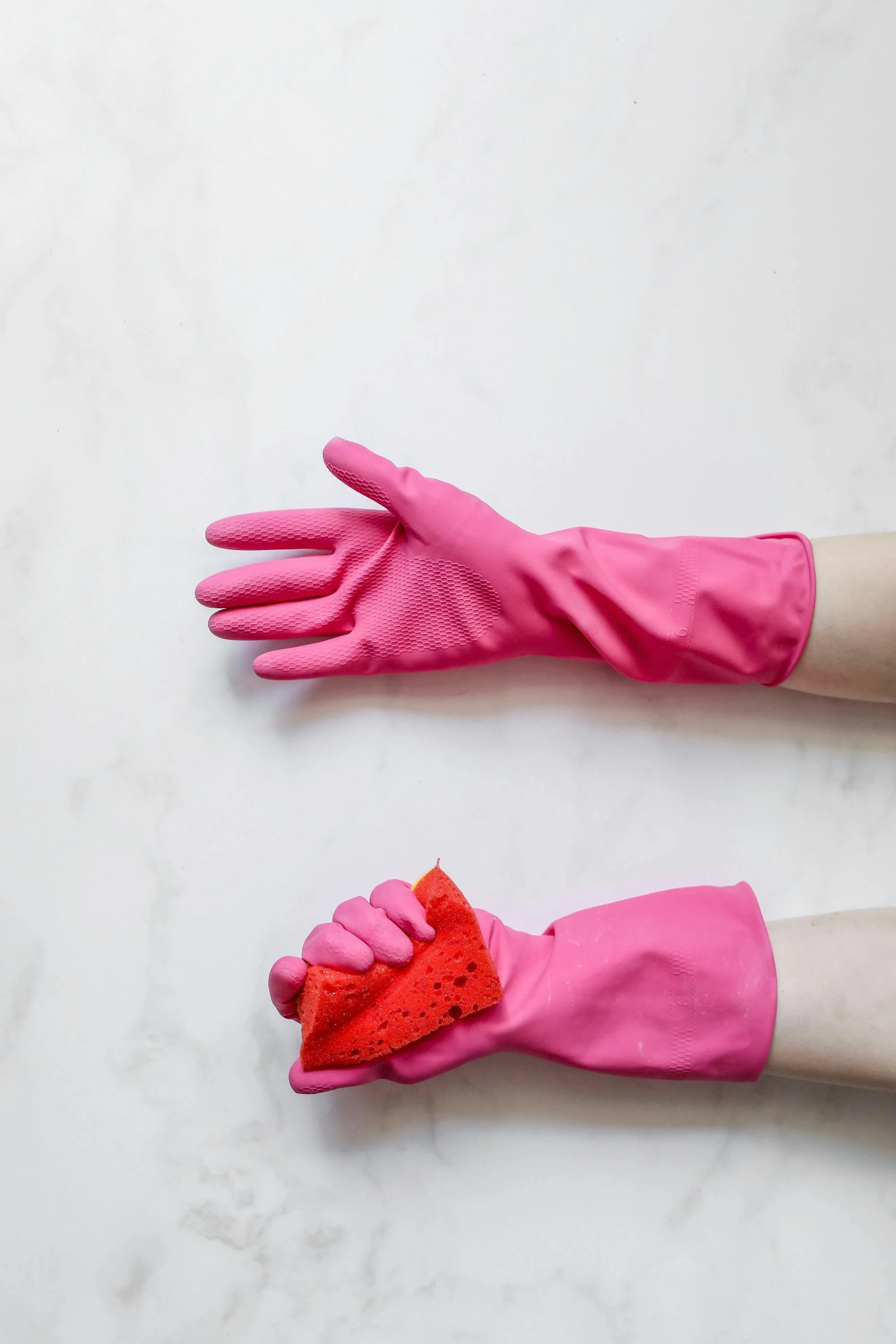 Two hands wearing pink rubber gloves. One hand holds a red cleaning sponge, the other hand is open and empty.