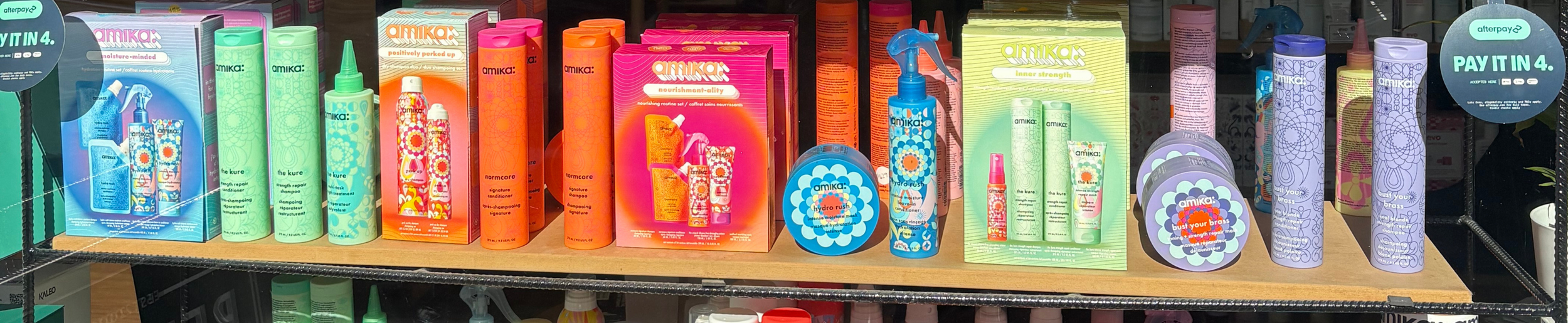 A shelf filled with various skincare and haircare products from the Amika brand, including shampoos, conditioners, sprays, and treatments in colorful packaging.