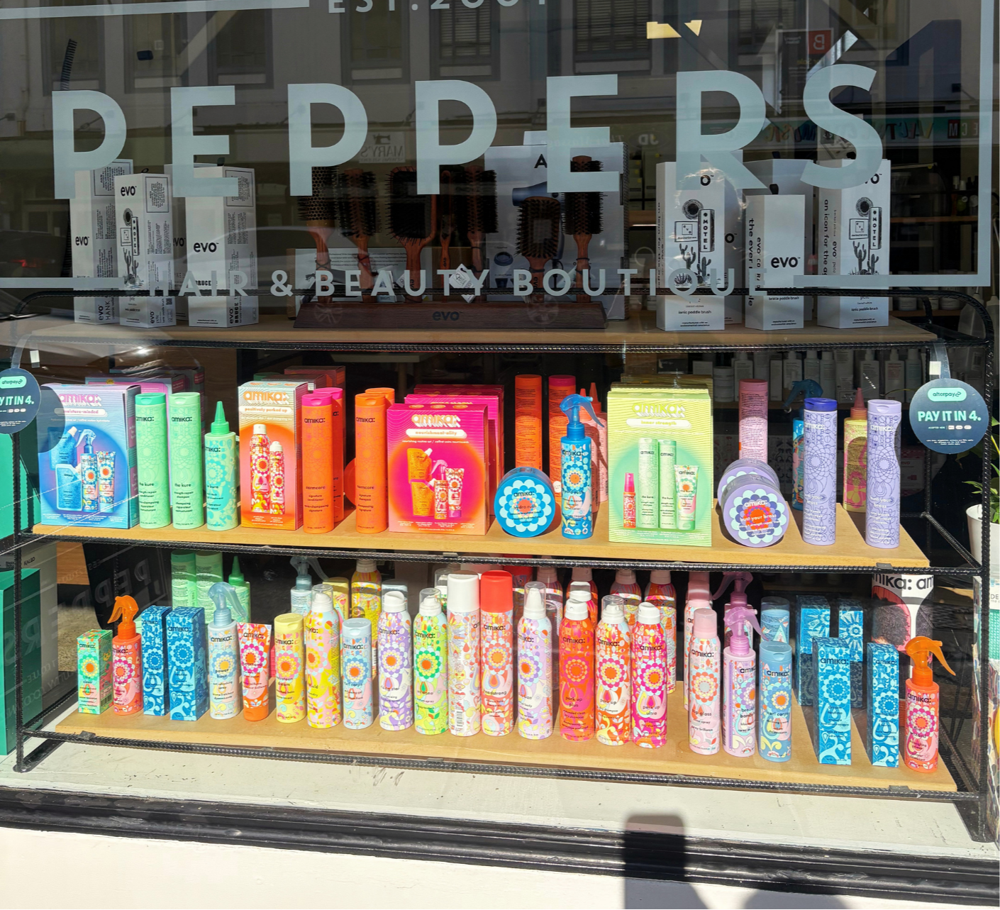 Display of colorful hair and beauty products in a store window with the sign 'PEPPERS' and 'HAIR & BEAUTY BOUTIQUE' on the glass.