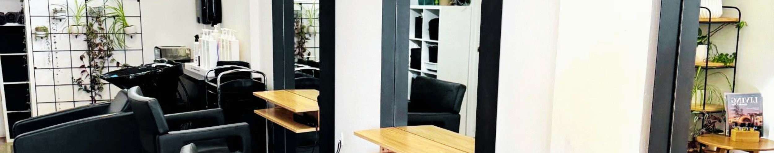 Modern salon or spa interior with black chairs, wooden tables, mirrors, plants, and shelving units.