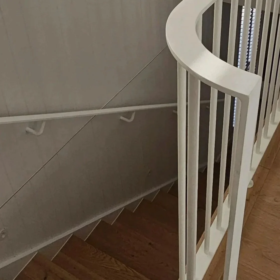View of a staircase with a white curved railing and wooden steps, viewed from the top.