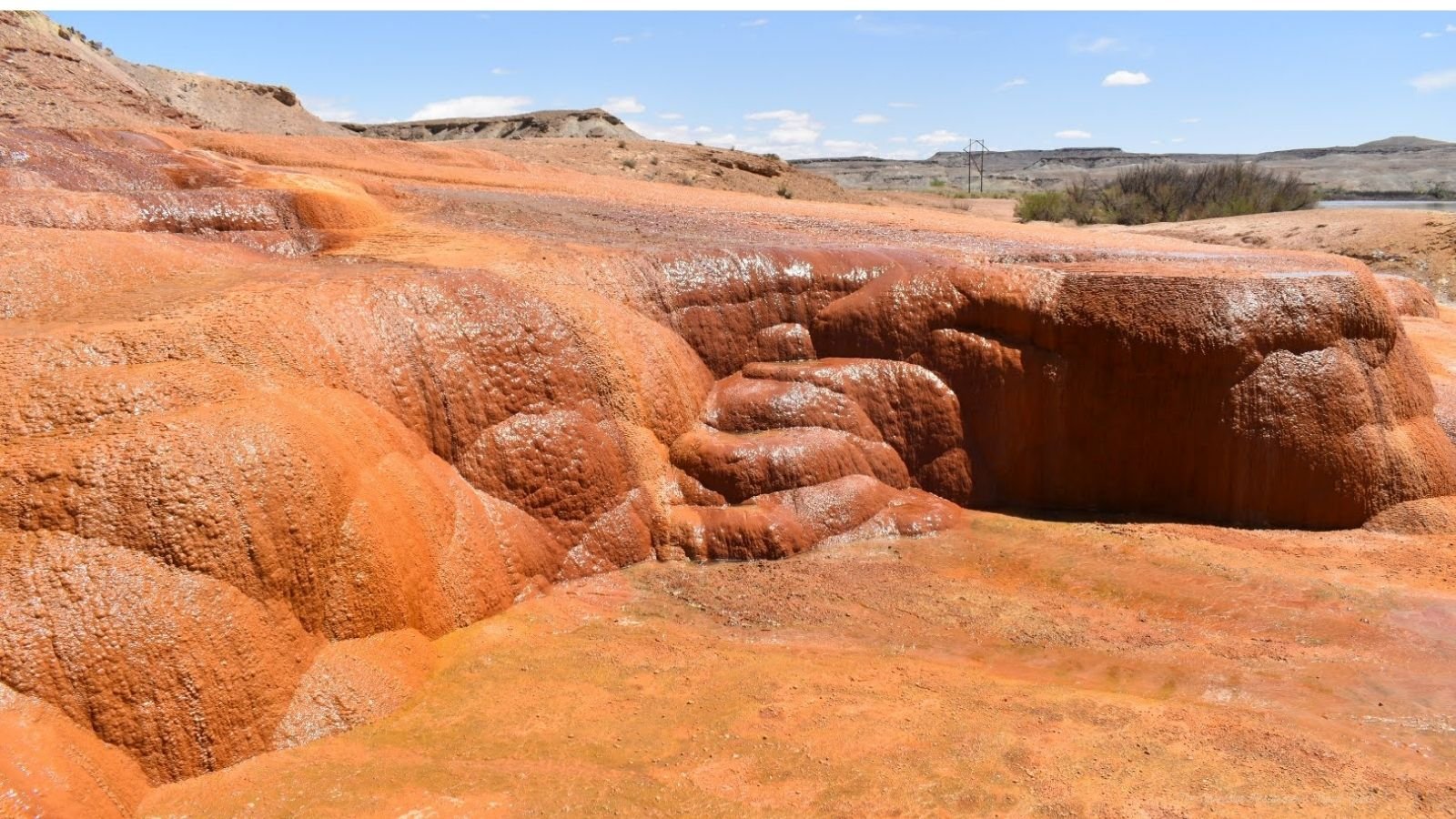 Red and orange layered rock formations in a desert landscape under a blue sky with scattered clouds.