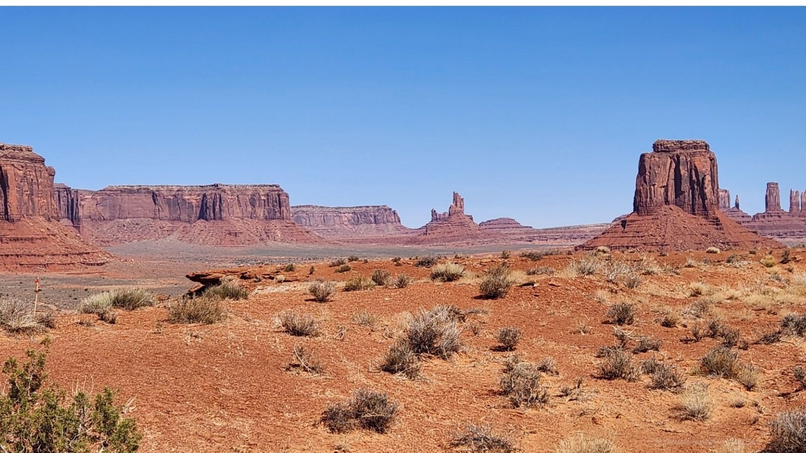 Desert landscape with red rock formations and sparse vegetation under a clear blue sky.