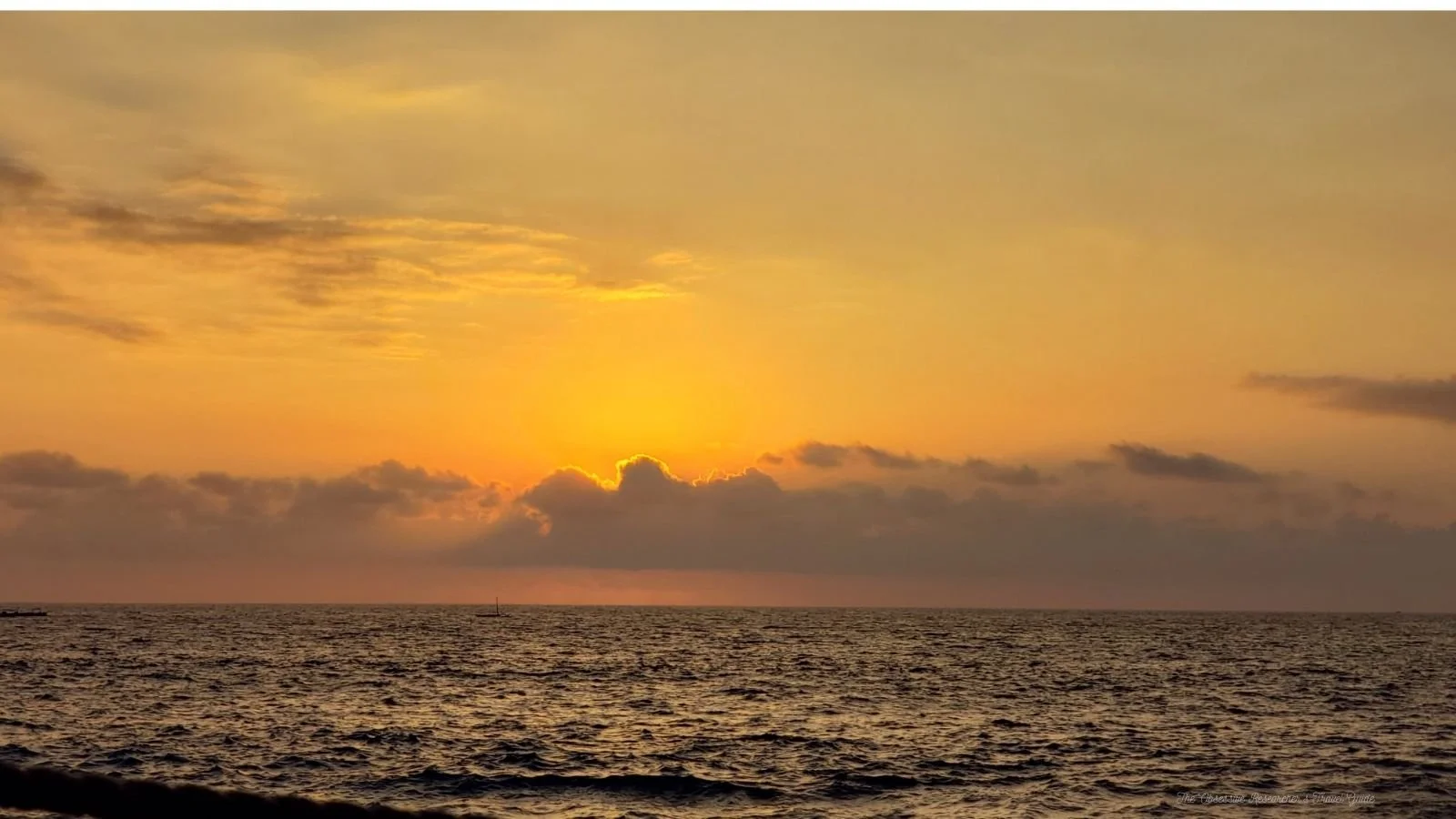 Sunset over the ocean with a partly cloudy sky, orange and yellow hues, and calm waves.