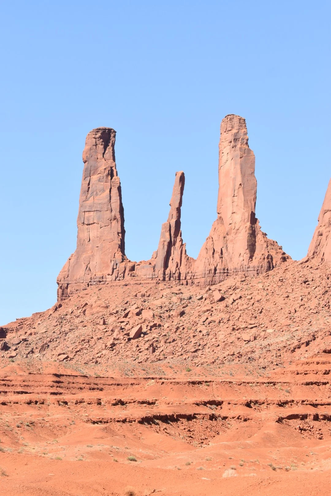 Three large red rock formations in a desert landscape against a clear blue sky.