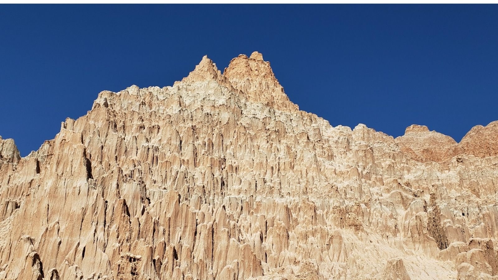 Close-up of a rugged, light-colored mountain with jagged peaks against a clear blue sky.