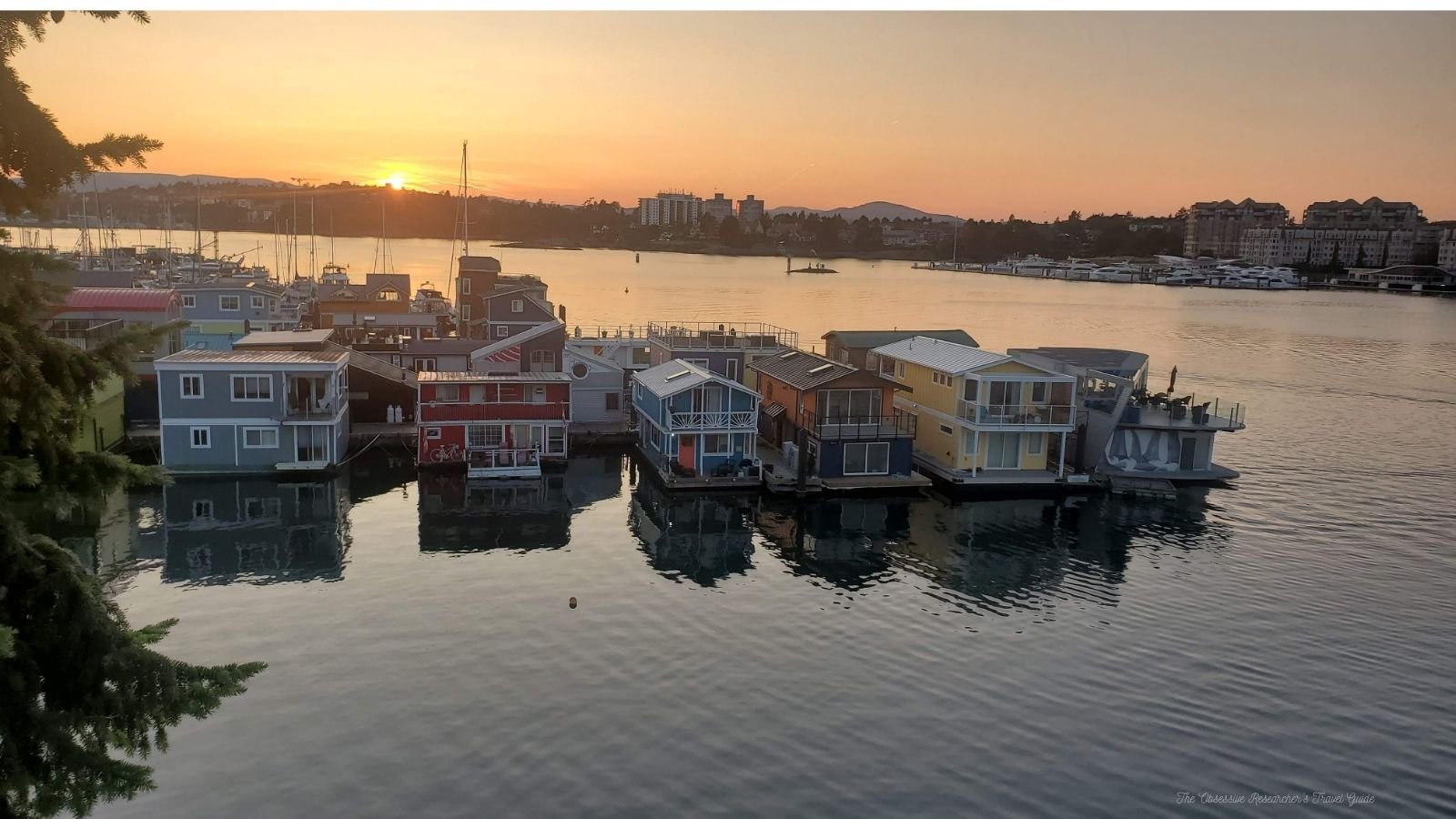 Colorful houseboats lined up along a calm waterway during sunset with boats docked at the marina in the background.