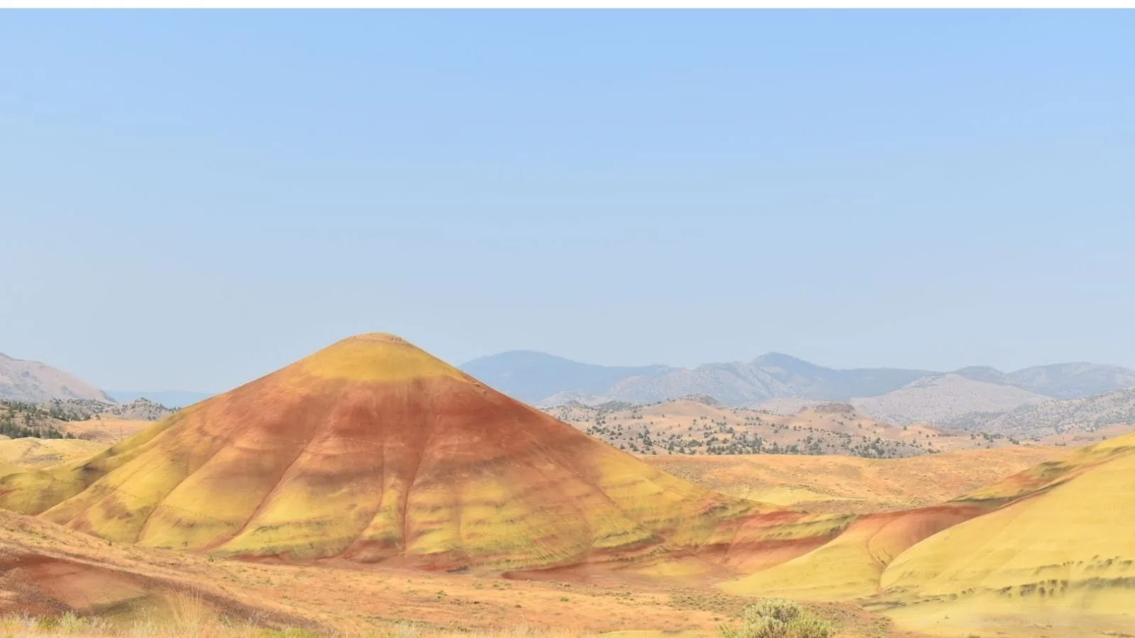 Colorful layered hills with yellow, red, and orange hues in a desert landscape under a clear blue sky.