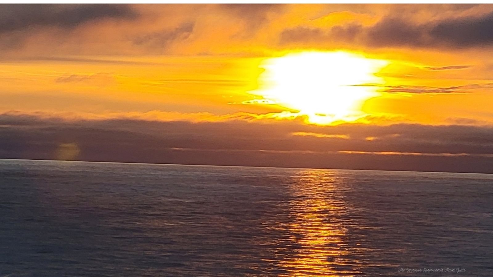 A sunset over the ocean with bright yellow and orange colors in the sky, reflected on the water surface.