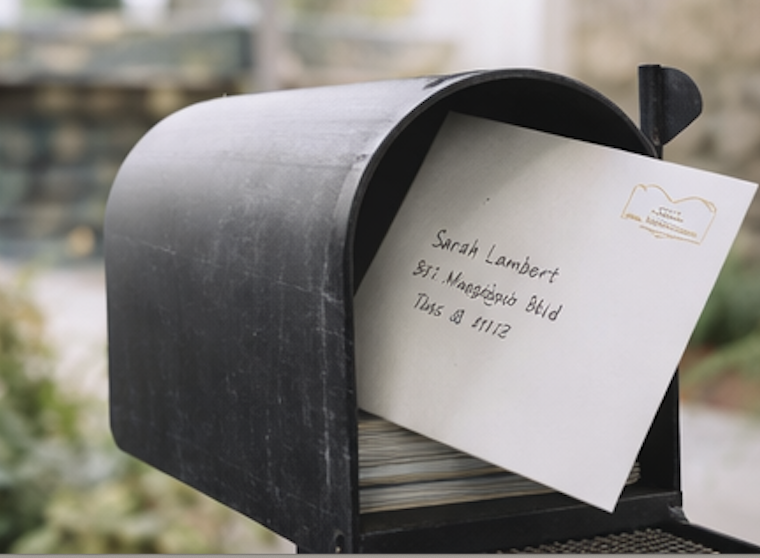 A black mailbox with an envelope partially inserted, addressed to Sarah Lambert at 871 Mangrove Blvd.