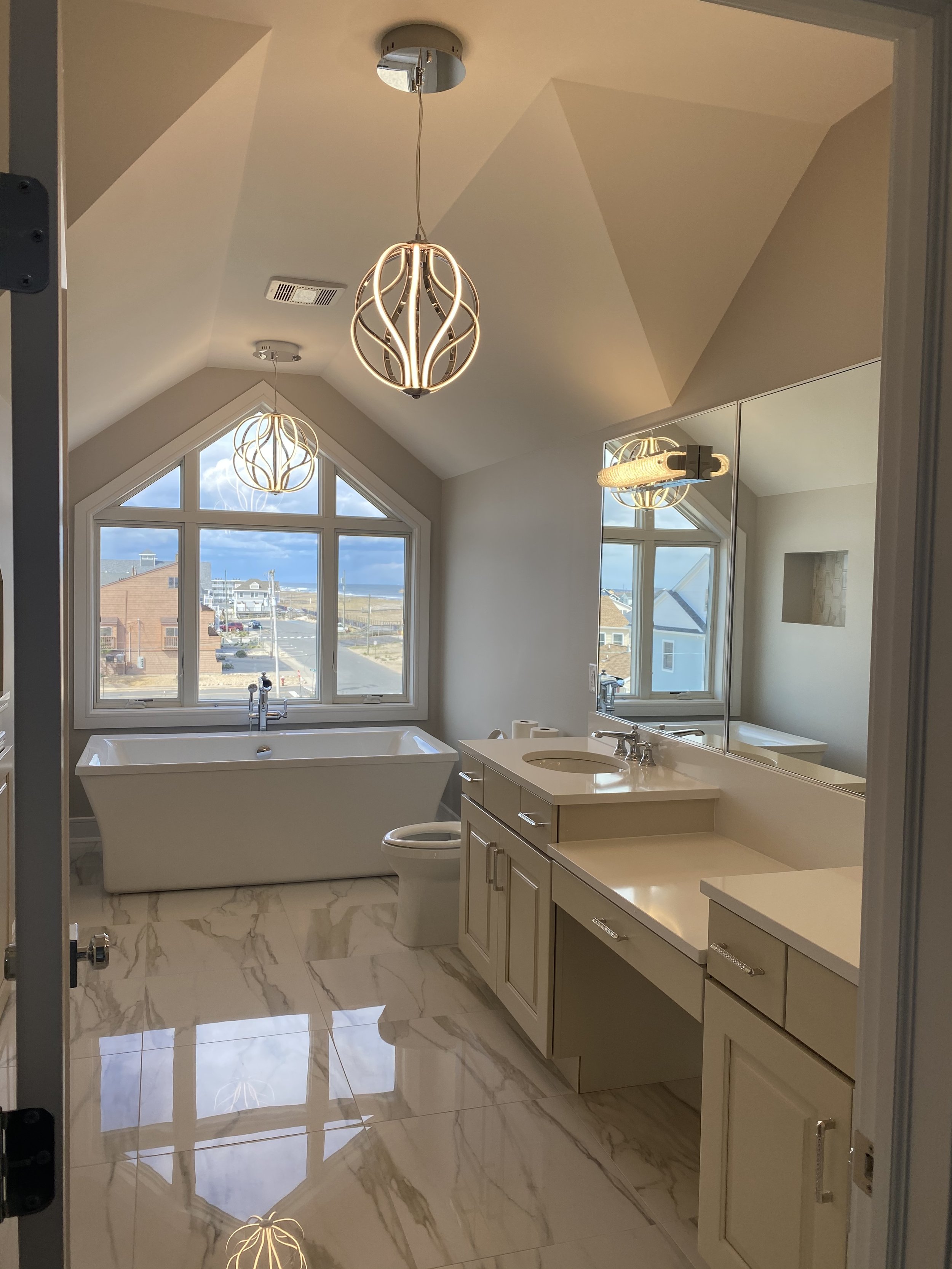 Elegant bathroom with freestanding bathtub, marble flooring, light cabinetry and large windows