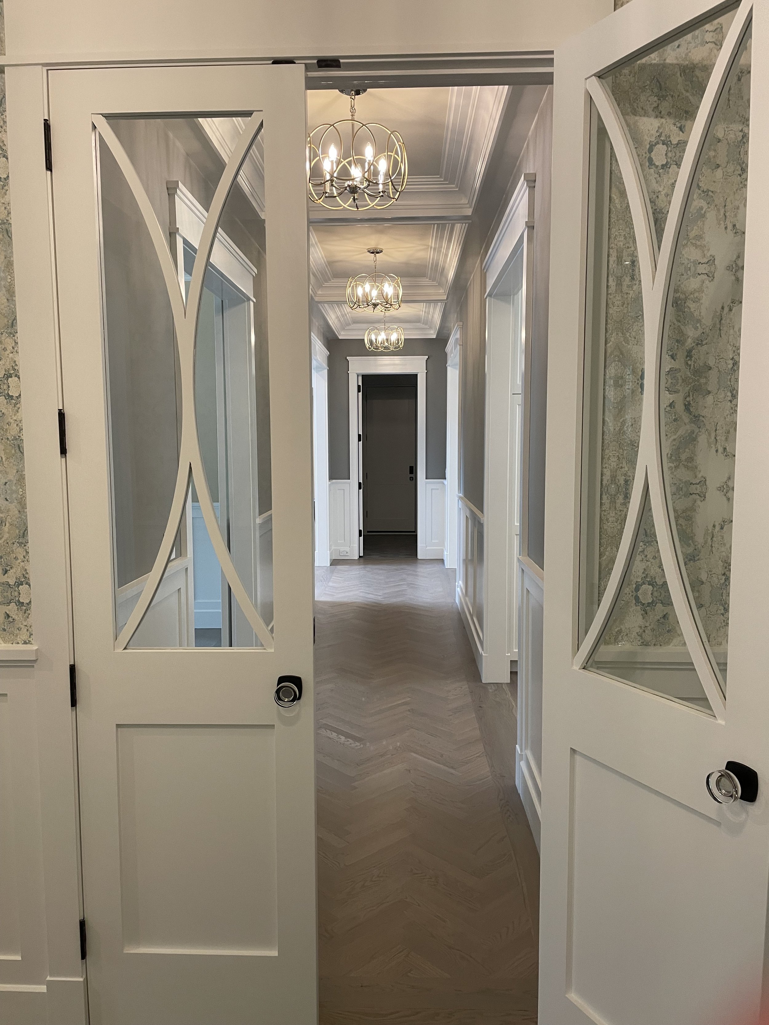 Elegant hallway with glass-paneled doors, chandeliers and herringbone wood floors