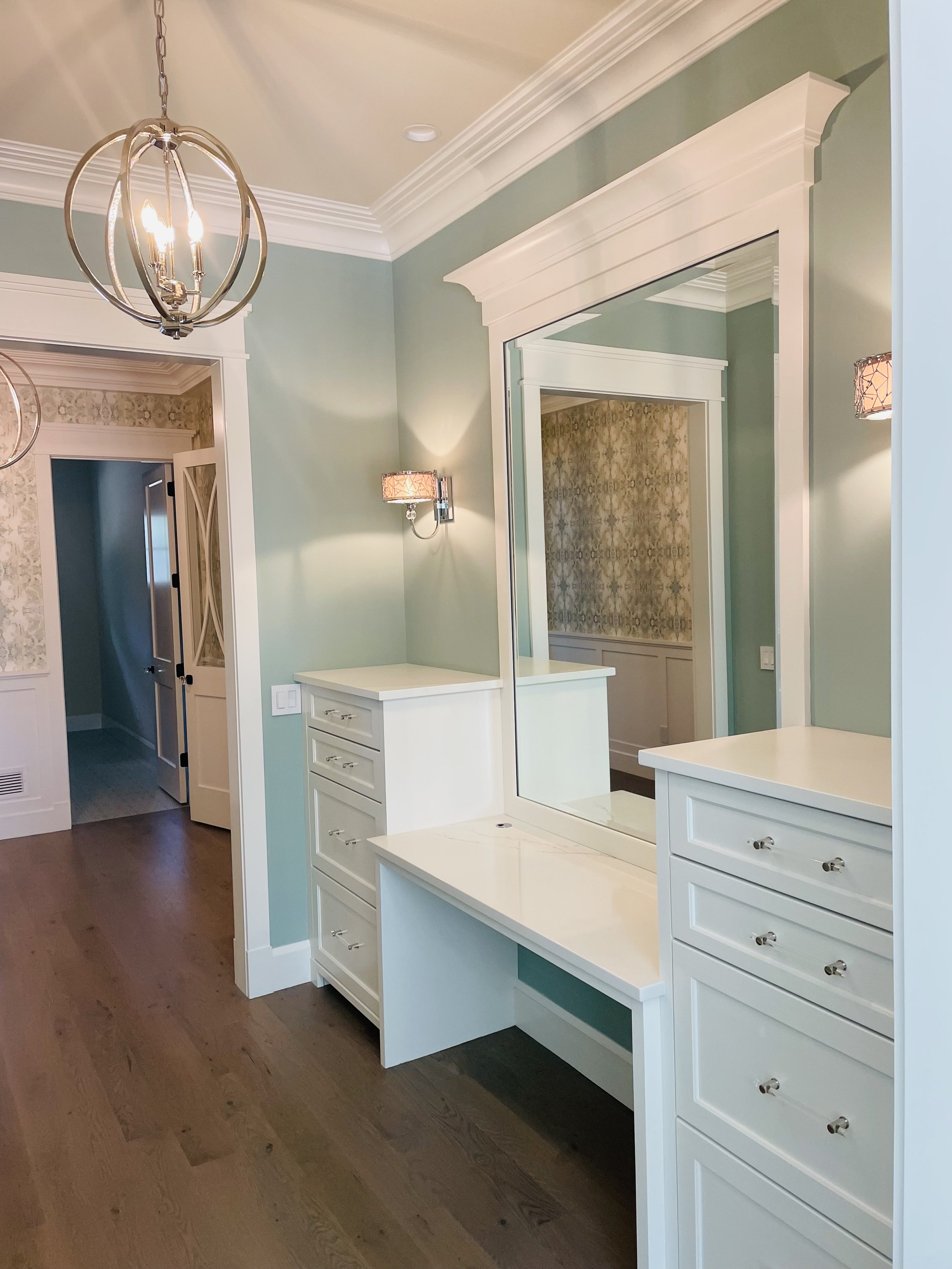 Pastel green interior with white cabinetry, large mirror and modern chandelier