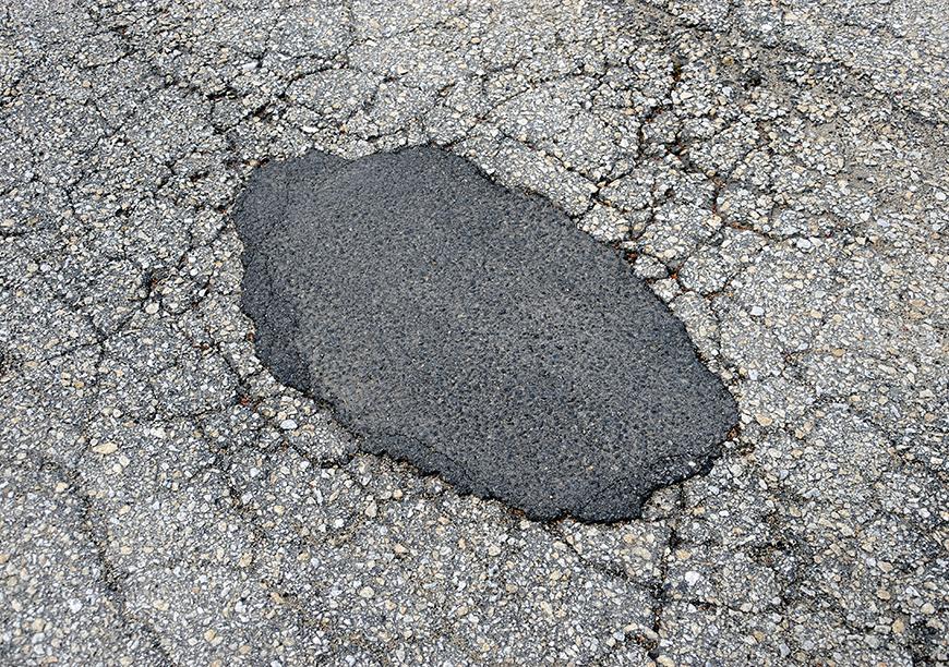 A pothole filled with asphalt on a cracked asphalt road.