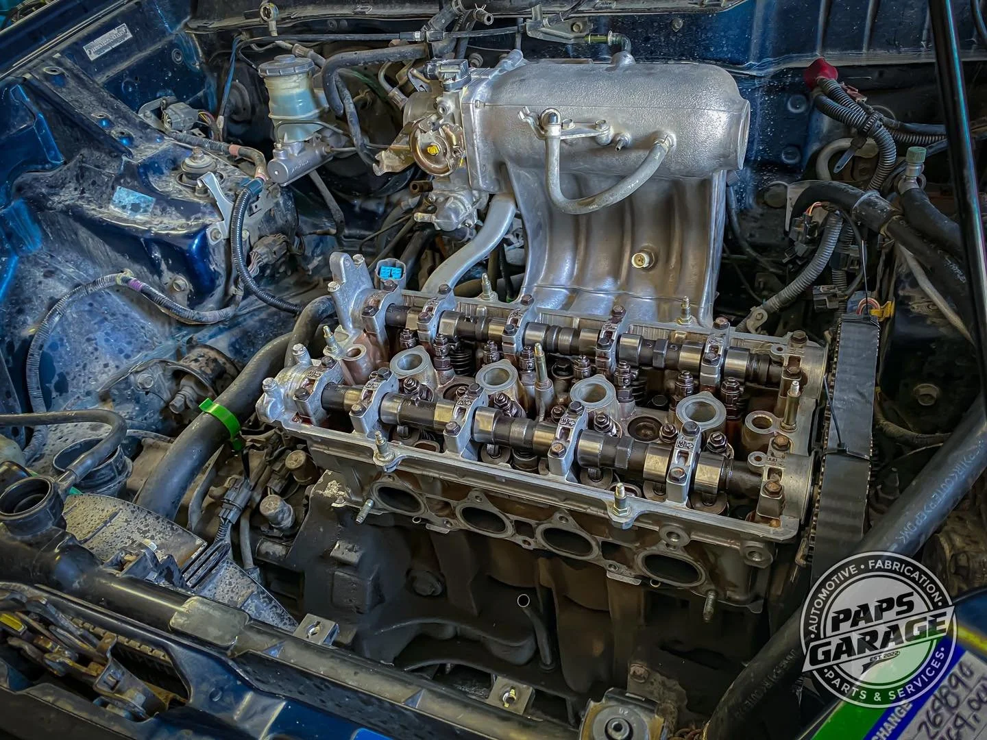 Under the hood of a car with the engine's cylinder head removed, revealing the camshaft and valve components.