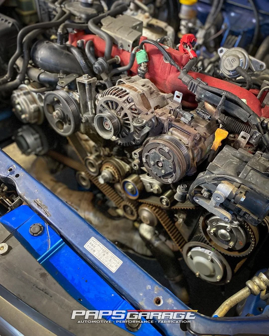 Close-up of a car engine with various belts, pulleys, and components visible.