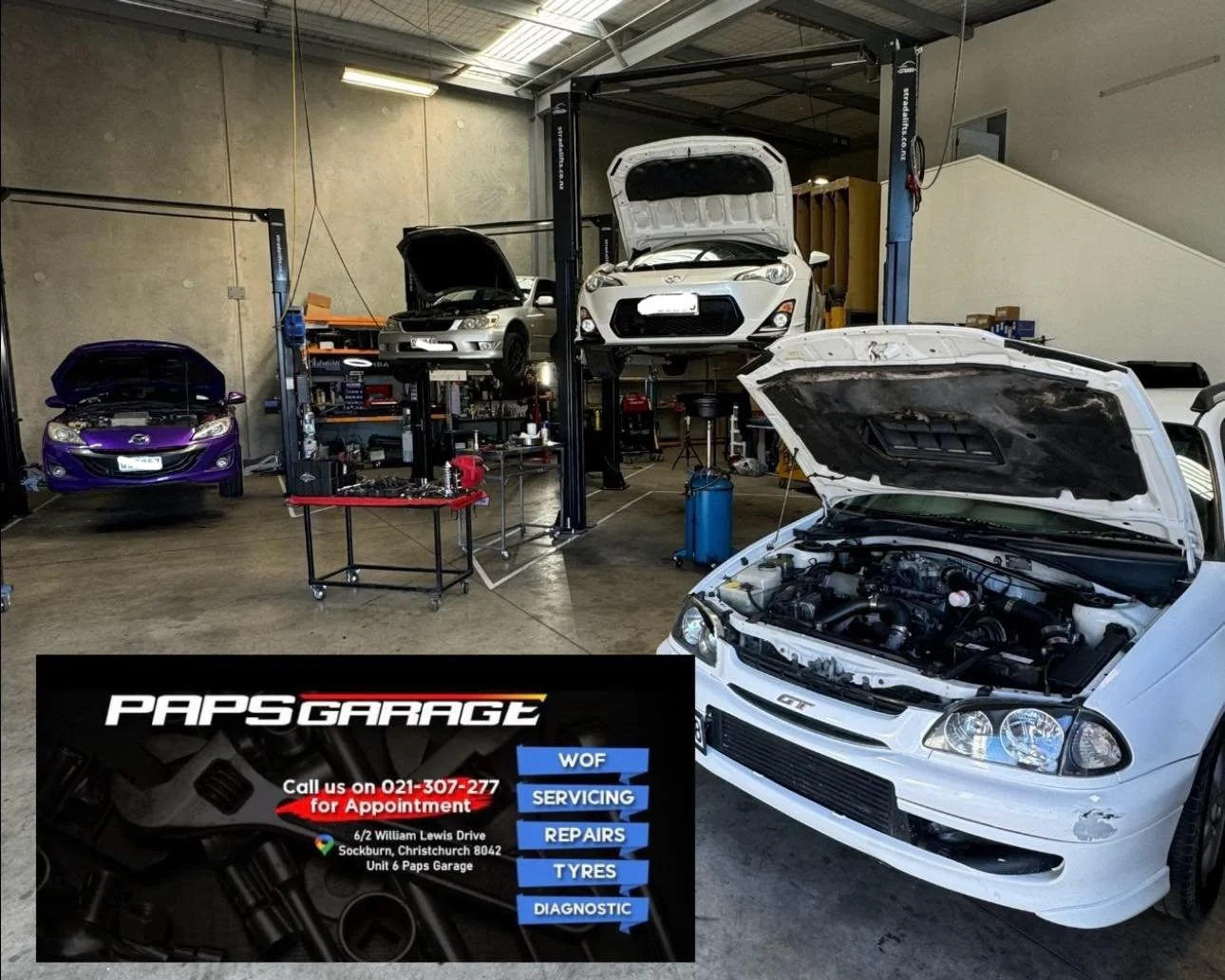 Inside an auto repair garage with multiple cars being repaired. A white car with its hood open is in the foreground, while a purple car is in the background. There are car lifts with cars elevated on them, and workbenches with tools. A sign for "Paps