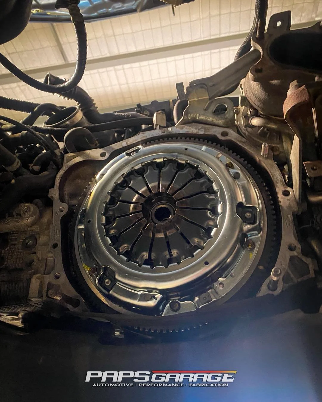Close-up of a car's engine with the transmission clutch assembly visible, indicating a repair or modification in progress.