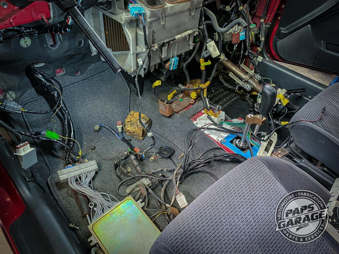 Interior of a car with removed seats, revealing exposed wiring, electronic components, and parts of the dashboard being disassembled.