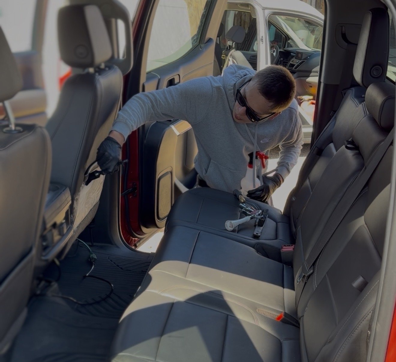 A person wearing black gloves and sunglasses working inside a red vehicle, possibly repairing or inspecting the backseat area.