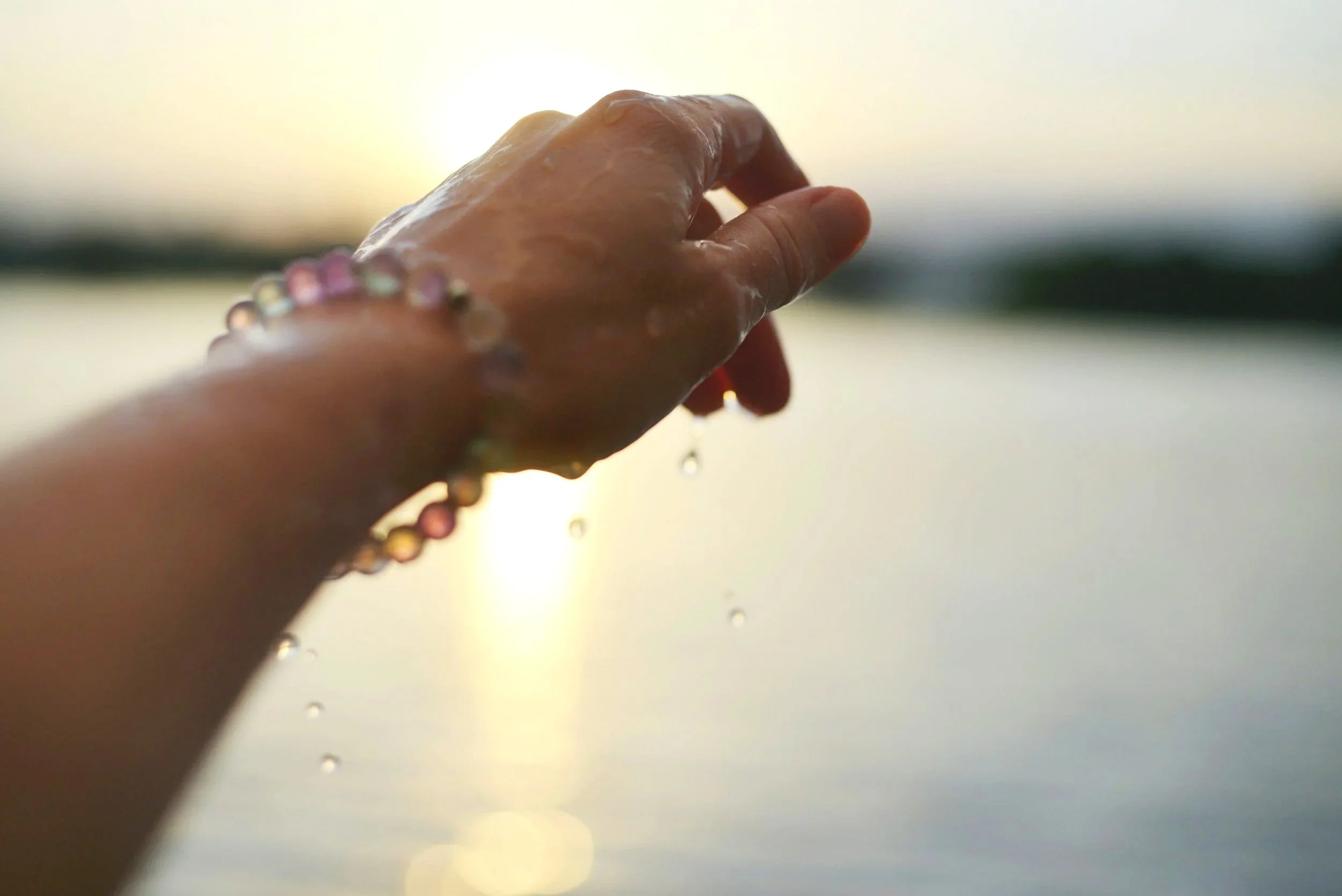 Sunlit hand with a crystal bracelet over water, symbolizing emotional release and healing through Regression to Cause Therapy.