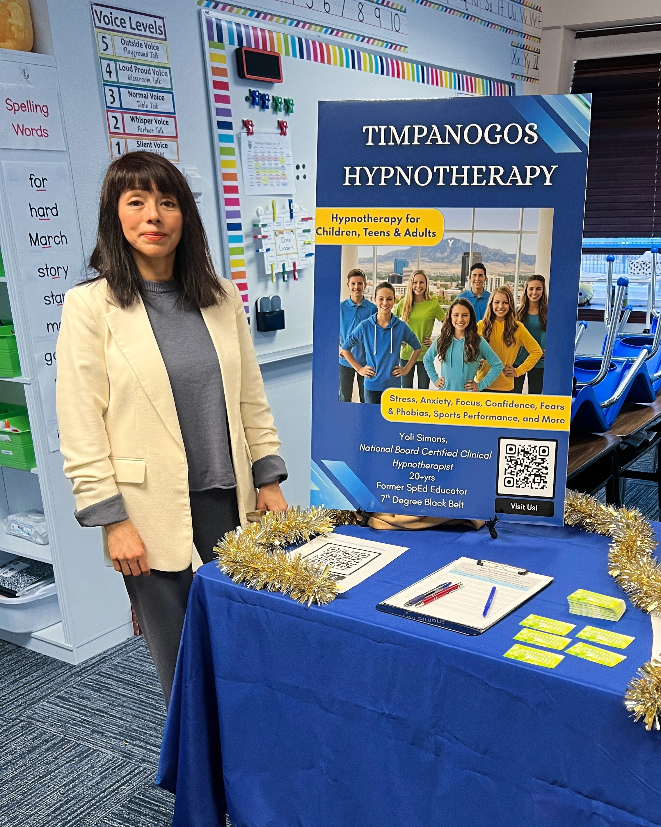 Yoli Simons standing by a Timpanogos Hypnotherapy display booth, offering anxiety and panic attack relief for children and adults.