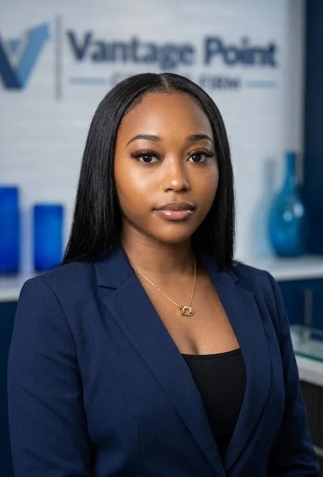 Professional woman with straight black hair in a navy blazer, standing in front of a blurred background with a sign that reads 'Vantage Point' and blue decorative vases.