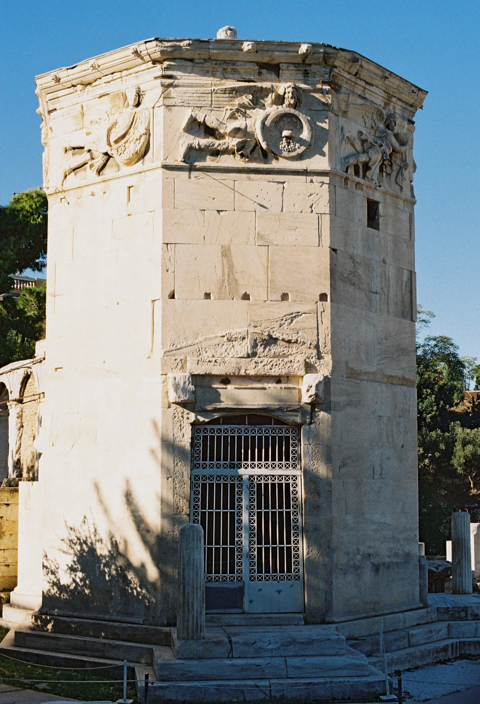 Ancient stone monument with decorative relief carvings at the top and a barred entrance at the bottom, surrounded by wooden posts and a small barrier.