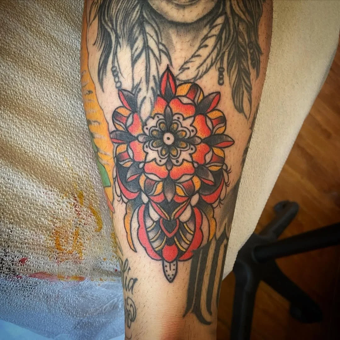 Colorful tattoo of a floral mandala design in red, orange, black, and white on a person's forearm.