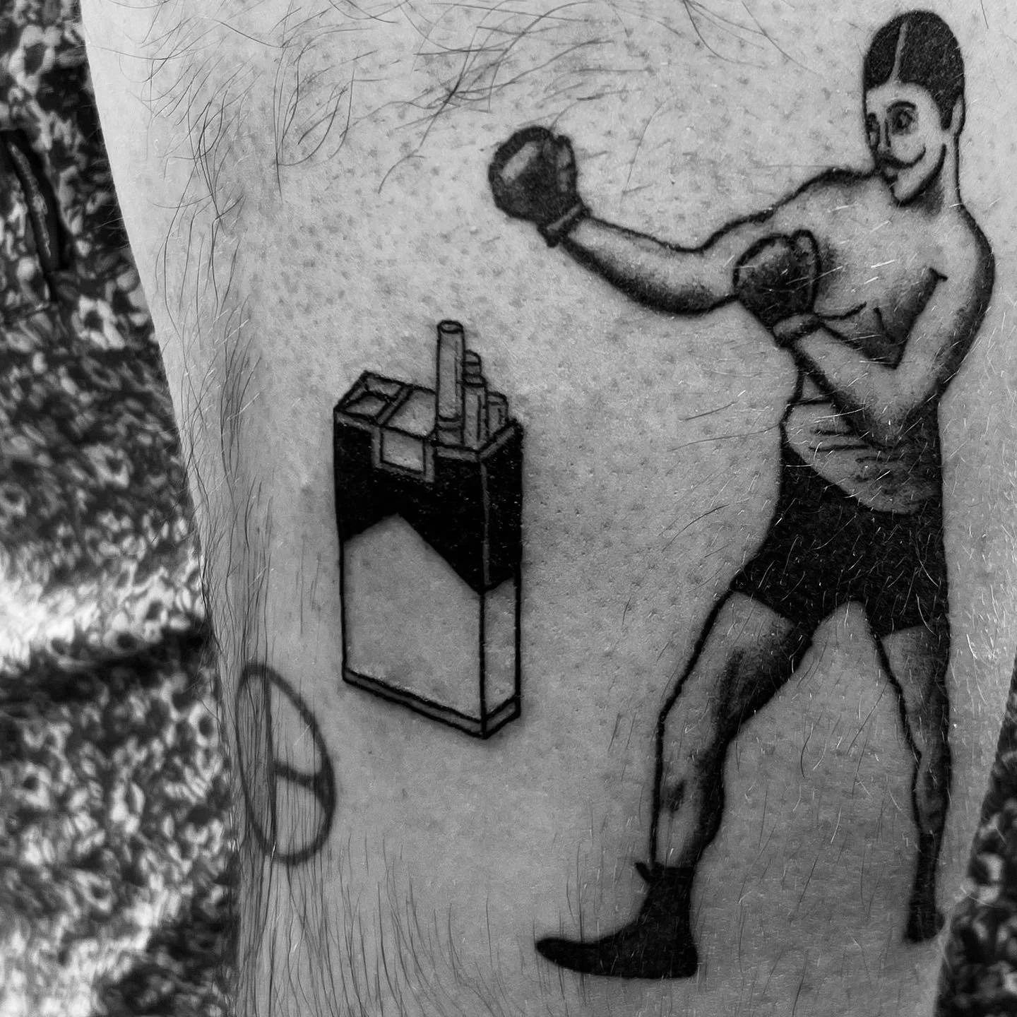 Tattoo of a boxer in a fighting stance with gloves on, next to a box of matches, on a person's skin.
