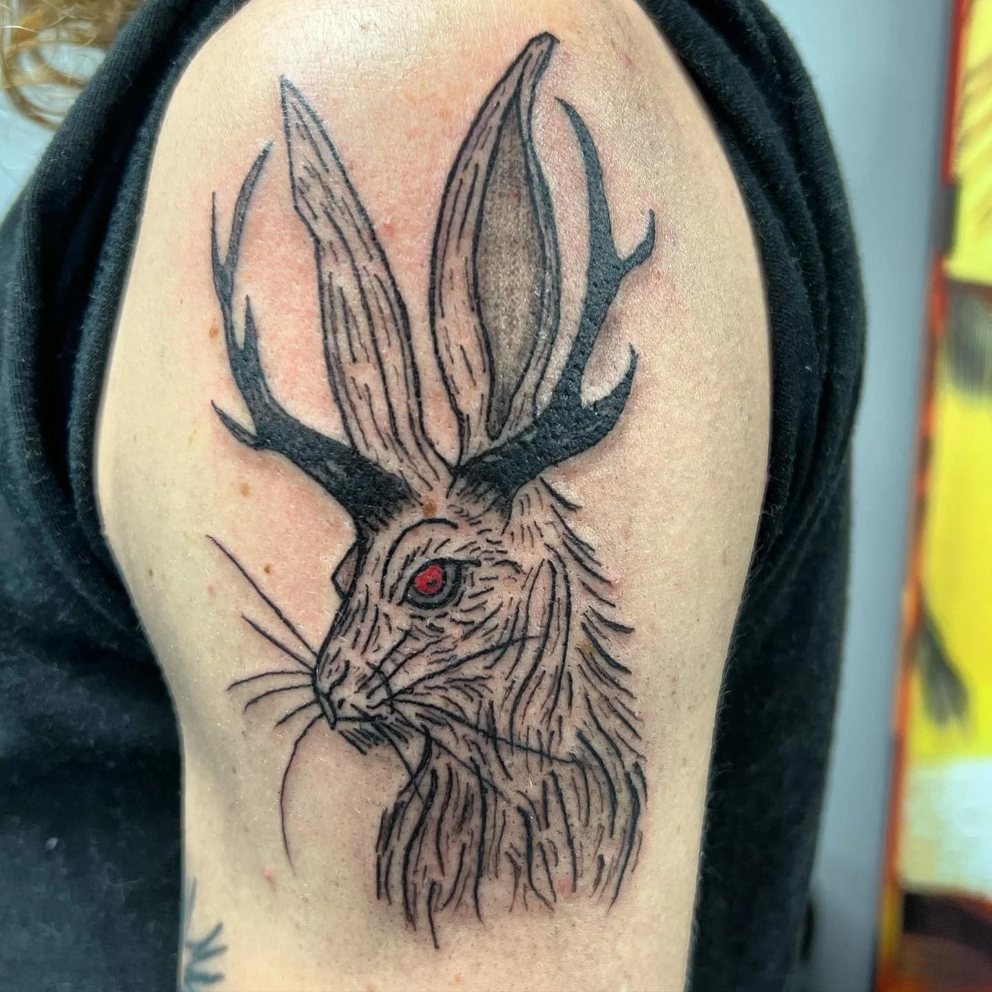 Tattoo of a hare with antlers and large ears, featuring detailed line work and a red eye.