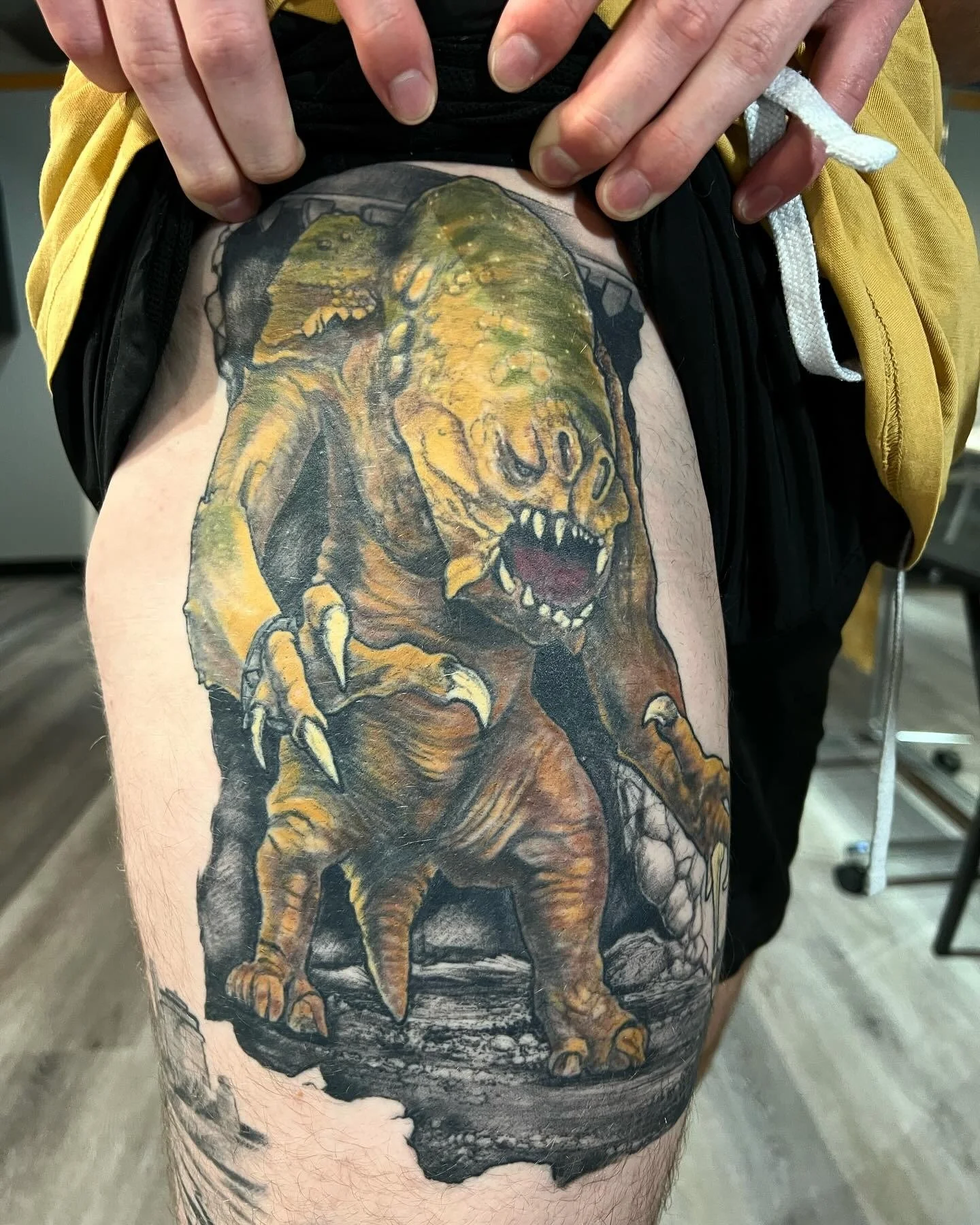 A detailed tattoo of a monstrous creature with a hyena-like head, sharp teeth, and claws, on a person's thigh.