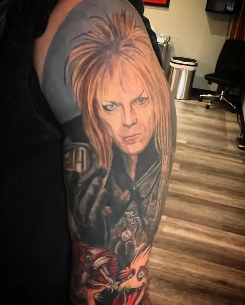 Tattoo of a woman with orange hair and piercing eyes on a person's upper arm, with a dragon and other elements below.