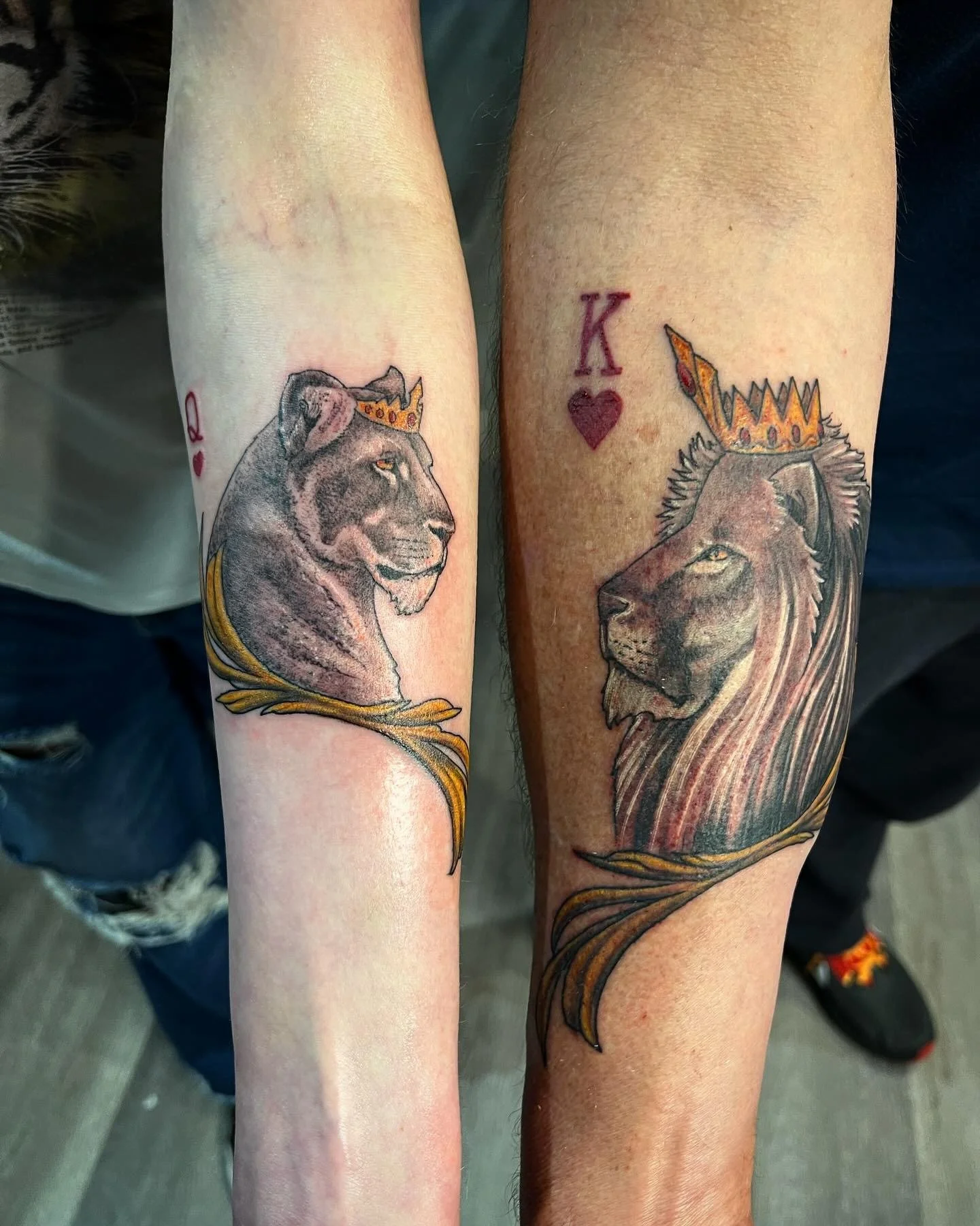 Tattoos of a lion and a lioness wearing crowns on their heads, with the lioness’s tattoo featuring a red heart and the letter K above it.