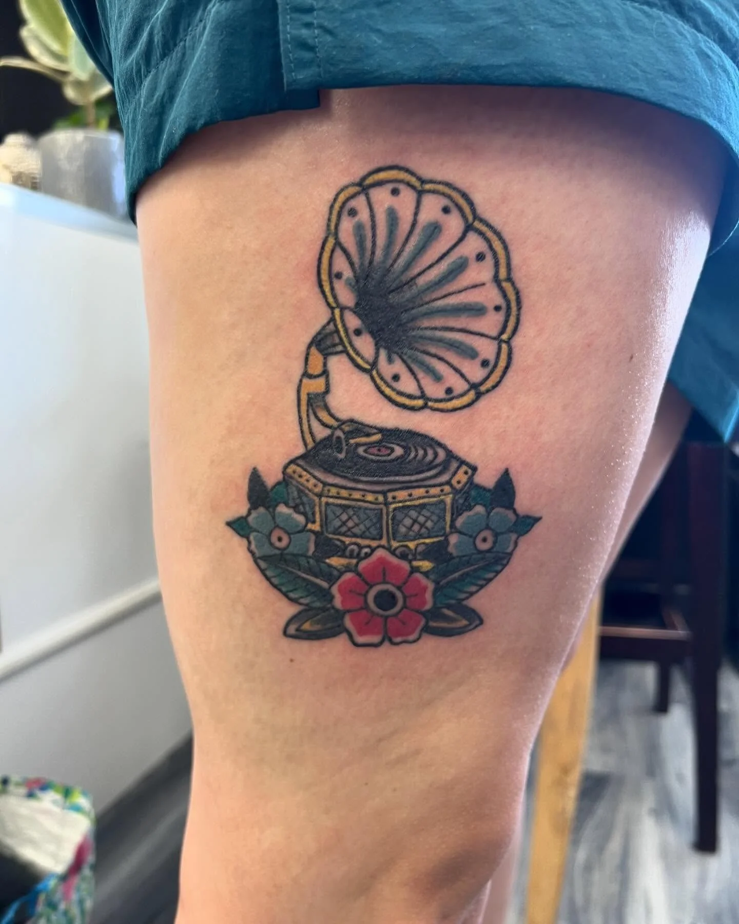 Tattoo of a vintage record player with a large flower beneath it, a gramophone horn, and decorative flowers surrounding the base.