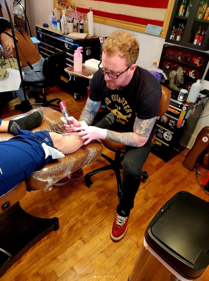 Tattoo artist working on a client's leg in a tattoo studio.