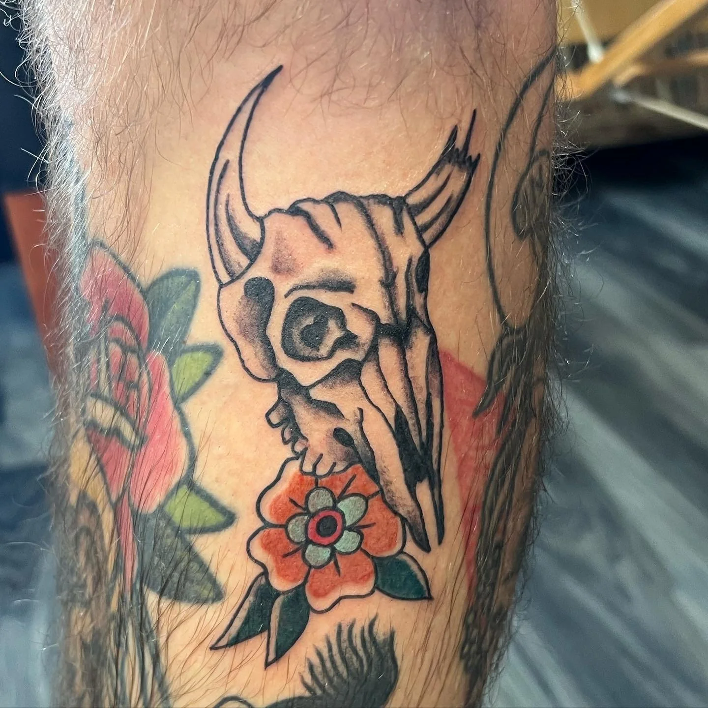 Tattoo of a deer skull with horns and a colorful flower below it.