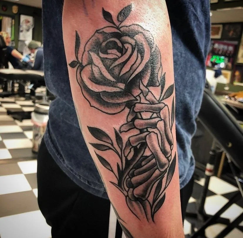 A tattoo of a skeleton hand holding a rose on an arm.
